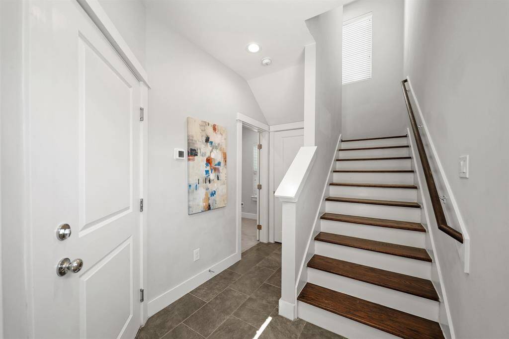 The foyer of the home with high ceiling and recessed lighting opens to a staircase with hardwood treadsleading to the second level of the home. The door to the left leads to the garage and the door in the background is the 3rd bedroom of the home.