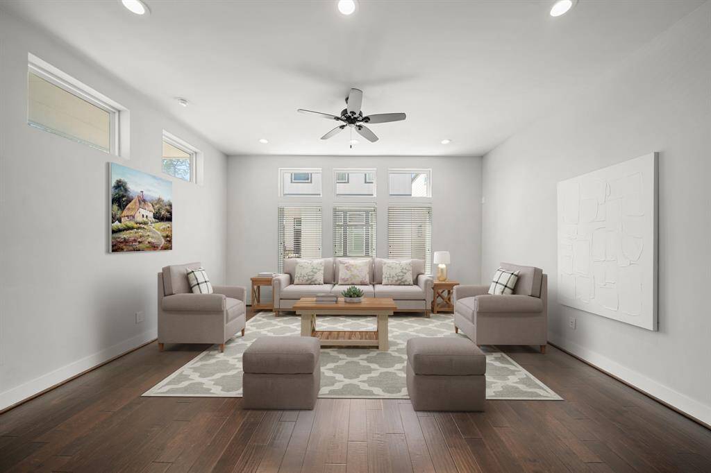 The living room includes a high ceiling with recessed lighting, a ceiling fan and gleaming hardwood floors.This photo has been virtually staged.