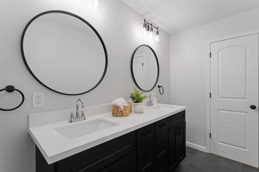The spacious secondary bathroom is designed for comfort and functionality. It features a large dual sink vanity with abundant cabinet storage and drawers, making it ideal for sharing. Overhead, large circular mirrors and modern vanity lighting enhance the space, adding both style and practicality.