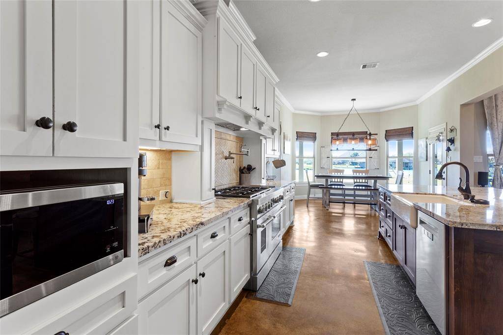 This spacious kitchen features elegant cabinetry, granite countertops, and stainless steel appliances. It offers a large island with a sink, ample storage, and a cozy dining nook with abundant natural light. Perfect for cooking and entertaining.