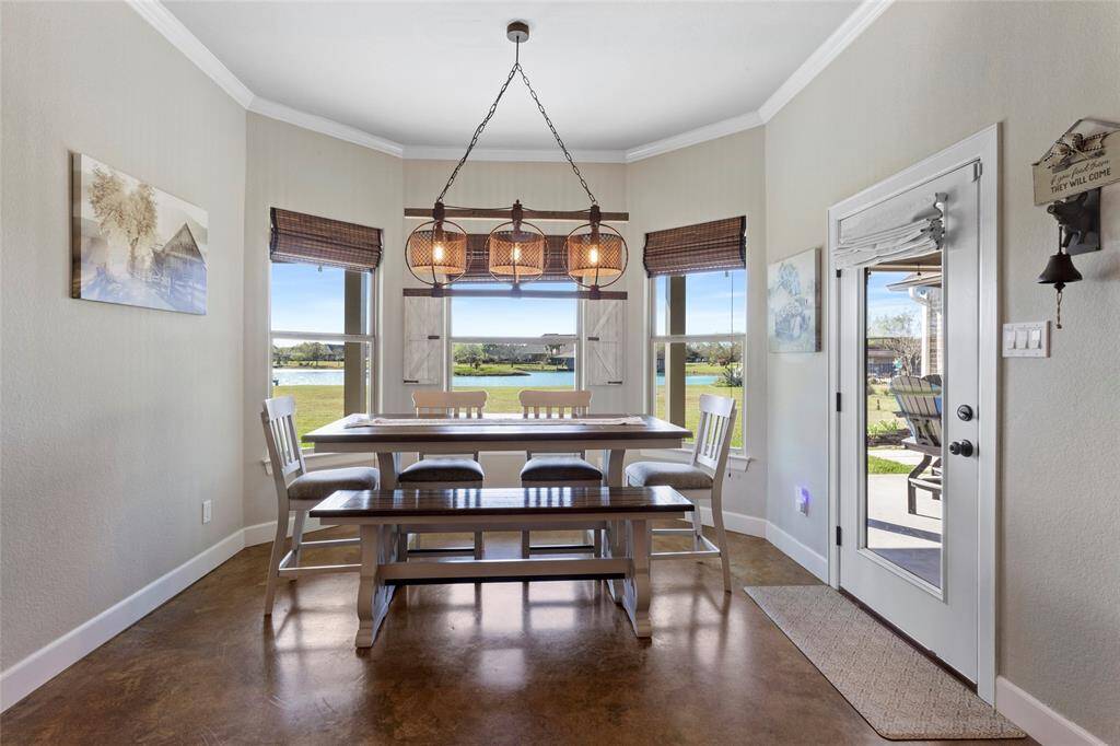 The dining area features large windows with a view of the lake, offering ample natural light. The farmhouse lighting is stylish and warm. The dining space opens to the patio through a glass door, enhancing indoor-outdoor living.