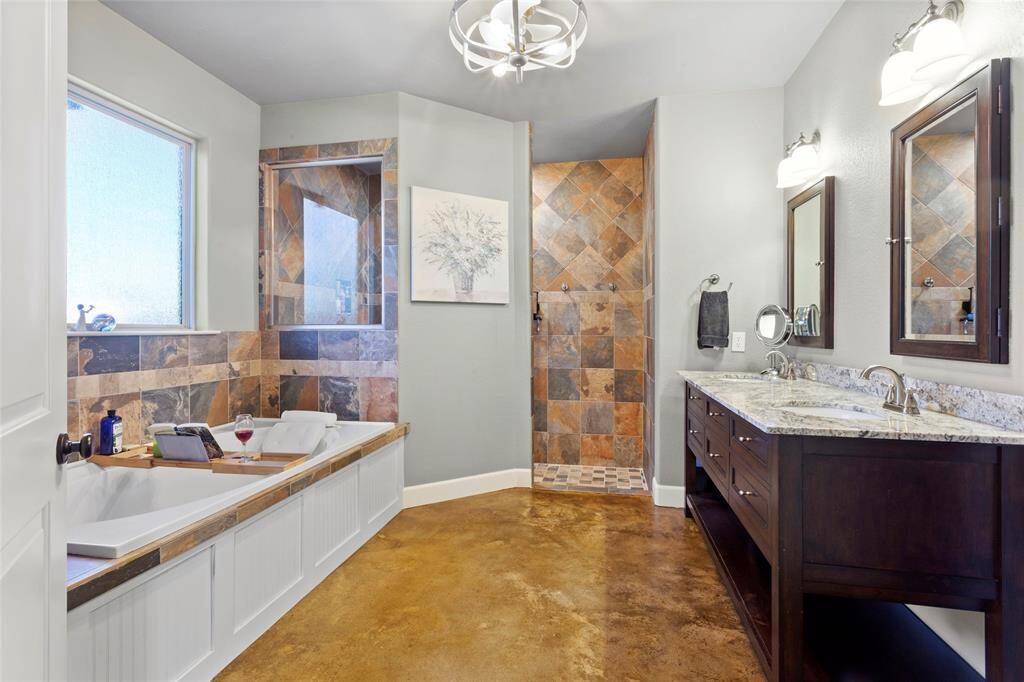 The primary ensuite bathroom features a spacious layout with a large soaking tub and a separate walk-in shower, both accented with custom tile work. It has a double vanity with granite countertops, modern fixtures, and ample storage. The room is well-lit, creating a relaxing and spa-like atmosphere.