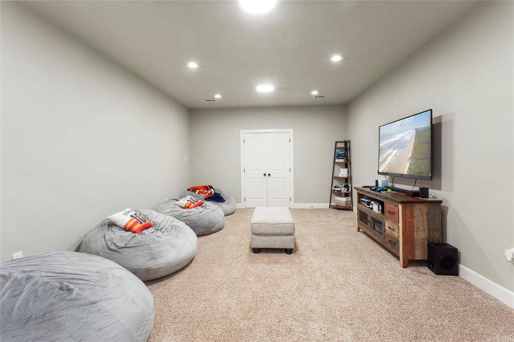 This upstairs cozy media room features plush carpet, ample seating space, and a large wall for a mounted TV or projector screen, perfect for relaxing and entertainment. The walk-in storage closet is great for blankets and movie night extras!
