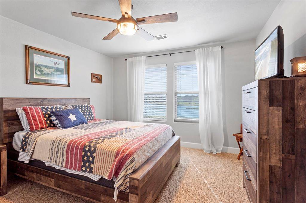 A cozy upstairs bedroom overlooks the lake. Natural light streams through two large windows, creating a bright and welcoming space to relax.