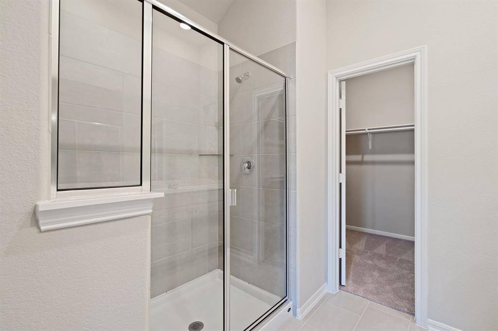 This additional view of your primary bathroom features tile flooring, fresh paint, large walk-in shower, and a large walk-in closet.