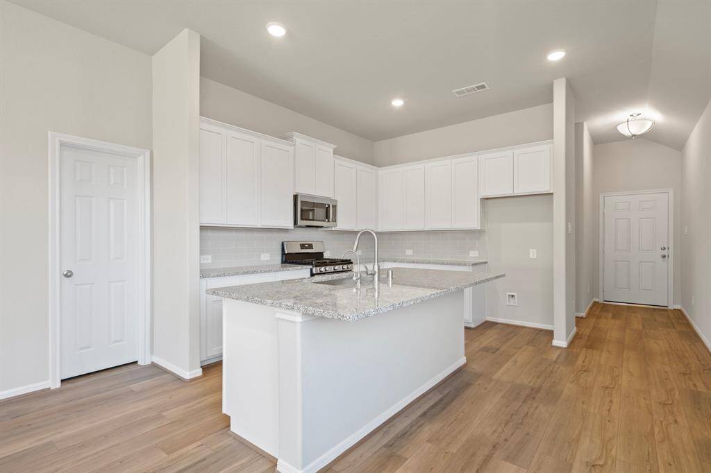 This light and bright kitchen features a large quartz island, white cabinets, a large sink overlooking your family room, recessed lighting, and beautiful backsplash.