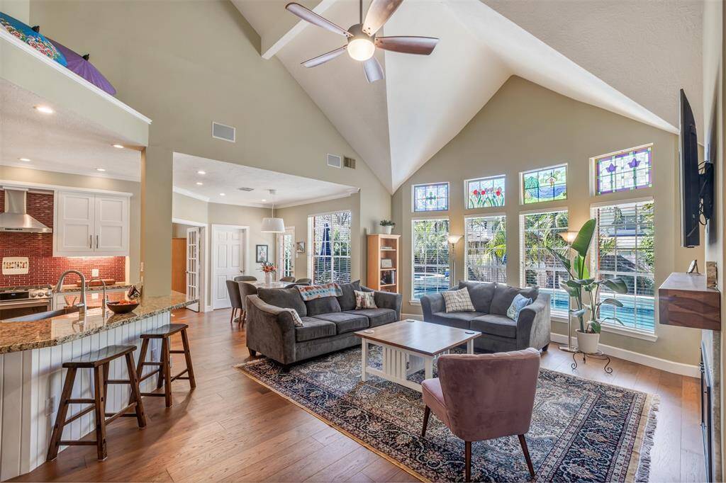 This large open floor plan has large windows that let's in lots of natural light. This pictures shows the spacious living room, breakfast area, and kitchen and you get a sneak peak at the gorgeous spa like backyard.