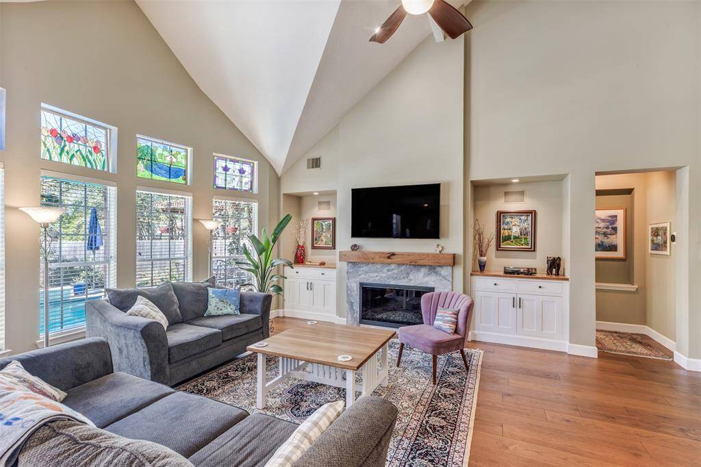 This photo shows the living room with high ceilings, large windows, updated fireplace surround, hickory mantel, gas fireplace with crushed glass. A local Master Craftsman built the storage cabinets and topped them with hickory tops to match the floors.