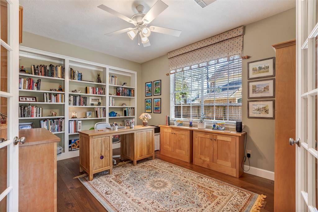 Here's a full view of the second home office. The beautiful hickory floors run throughout this space. This room contains large windows, wood blinds, window valence, built in shelving on the back wall, and a ceiling fan.