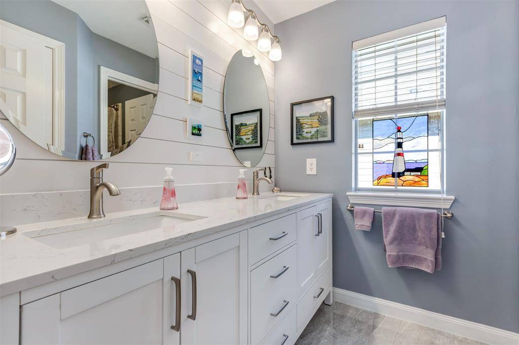 This bright family bathroom has been updated with fresh paint, new vanity with dual sinks, quartz counters, ship-lap accent wall, tile, shower bath combo, and lighting.