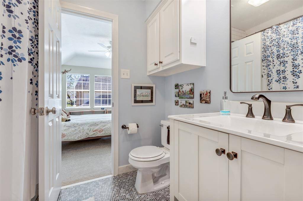 This picture shows the ensuite bathroom. It contains a bath/shower combination, new vanity and sink, tilework, toilet, and storage above the toilet.