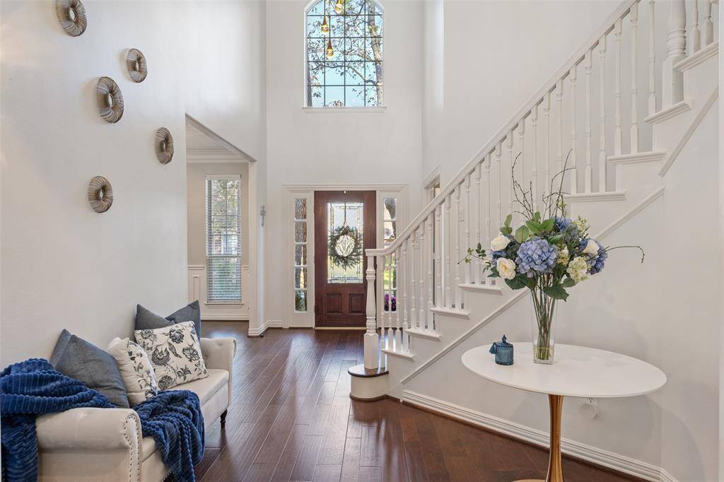 This inviting entryway features elegant hardwood floors leading to a grand wooden curved traditional-style staircase. The open layout includes a cozy sitting area and ample natural light, creating a welcoming atmosphere. French doors open to a home office, adding functionality and charm.  Note the soaring ceilings throughout this beautiful home.