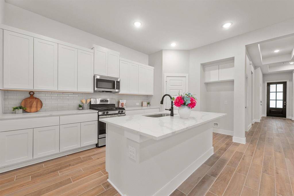 Featuring a large central island, tile backsplash, beautiful white cabinetry, and ample counter and cabinet space.