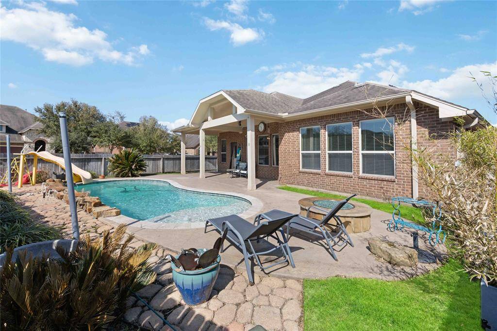 The backyard features a covered patio, a pristine swimming pool with a slide, and a cozy seating area. Perfect for outdoor entertaining and relaxation.