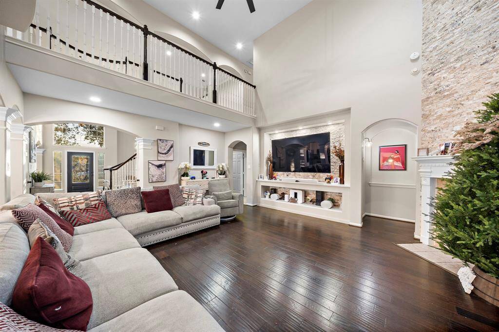 Experience grandeur in this spacious living room, featuring a two-story layout with an impressive view of the open balcony above. The thoughtfully designed built-in entertainment niche and stone fireplace blend modern convenience with timeless charm, creating a space that’s both functional and stunning.