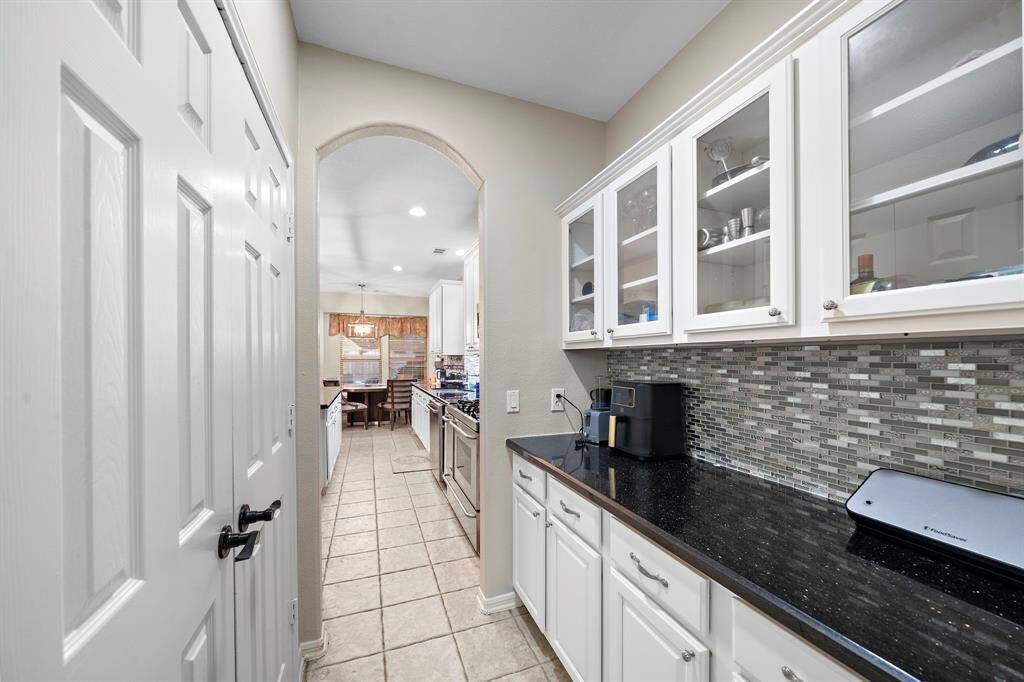 This stylish butler’s pantry provides added functionality and elegance, featuring granite countertops, glass-front cabinetry, and a modern backsplash. It’s an ideal space for additional storage, prep work, or a convenient coffee station.