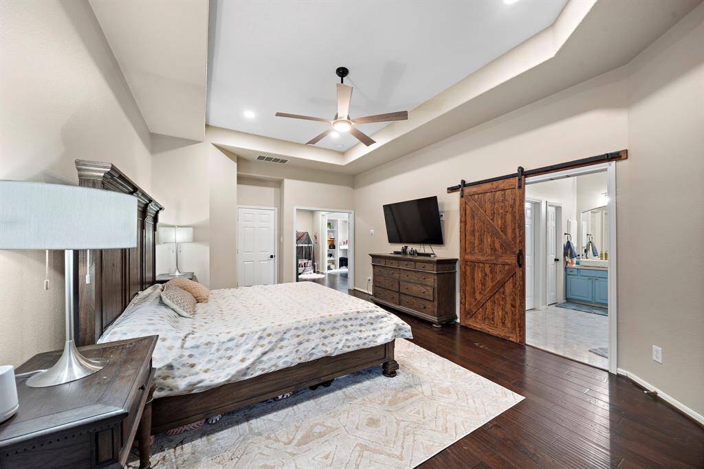 A custom barn door adds charm and privacy to this spacious primary bedroom, seamlessly connecting it to the luxurious ensuite bathroom and adjoining flex space.