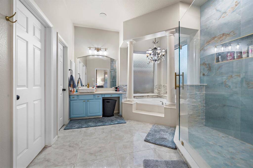 Step into a spa-like primary bathroom adorned with stunning finishes, including a soaking tub framed by decorative columns, a custom chandelier, and a spacious walk-in shower with modern tilework.
