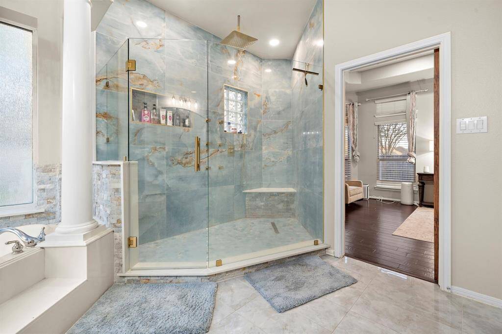 The oversized walk-in shower is a showstopper, showcasing exquisite tile work, a built-in bench, and sleek gold fixtures that exude elegance.