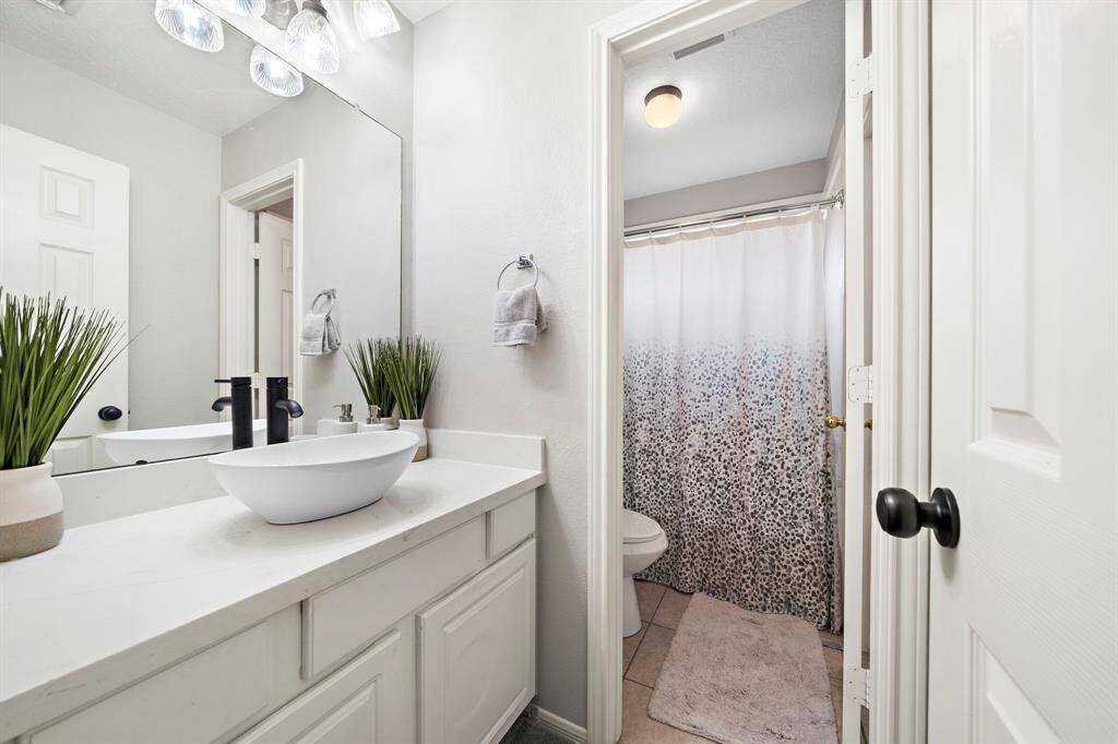 A thoughtfully designed bathroom featuring a stylish bowl sink and elegant mirror. The well-lit shower area adds functionality to the sleek and contemporary layout.
