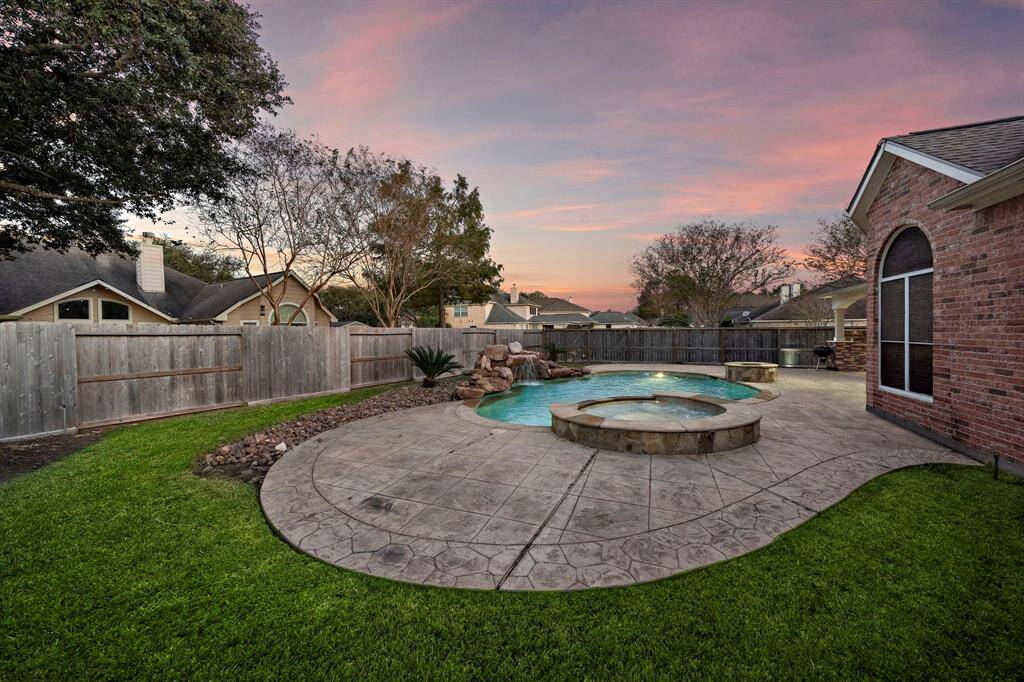 A waterfall feature flowing into the pool creates a peaceful ambiance, while the expansive stamped concrete patio provides plenty of room for outdoor seating.