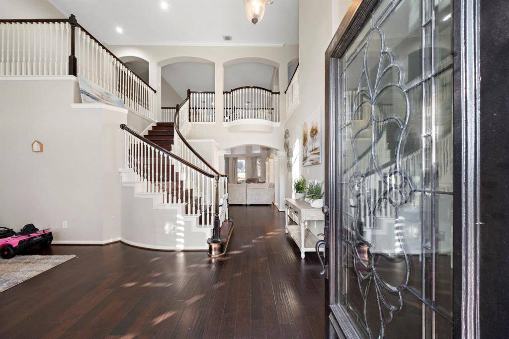 The entry showcases custom architectural details, with a graceful staircase leading to the second floor. Natural light streams through the decorative glass entry door, adding to its charm.