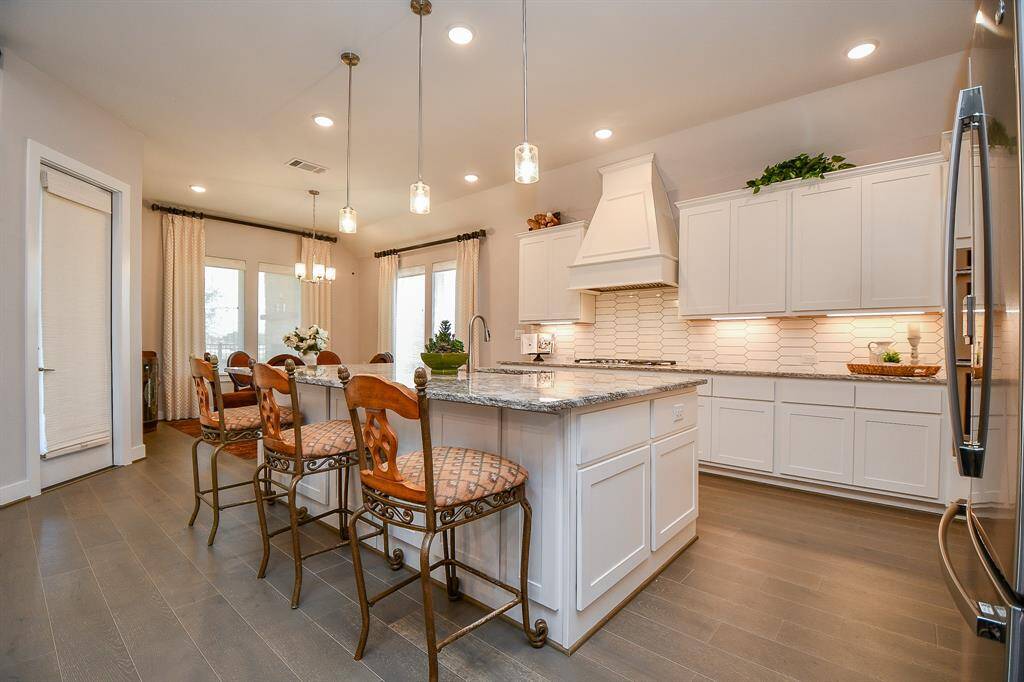 This kitchen features a modern design with white cabinetry, granite countertops, and stainless steel appliances. A large island with bar seating is illuminated by pendant lights, while an adjacent dining area offers additional space for entertaining.