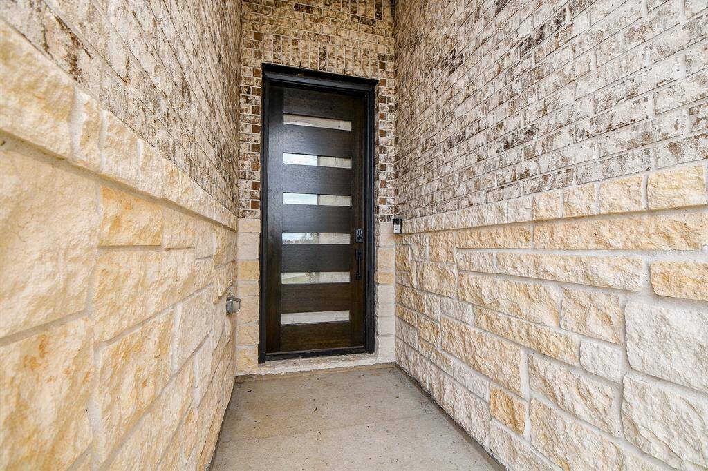 Your guests will stay out of the weather as they enter this modern entryway with a dark wood door featuring frosted glass panels. The surrounding walls are a mix of light stone and brick, creating a welcoming and stylish entrance to the home.