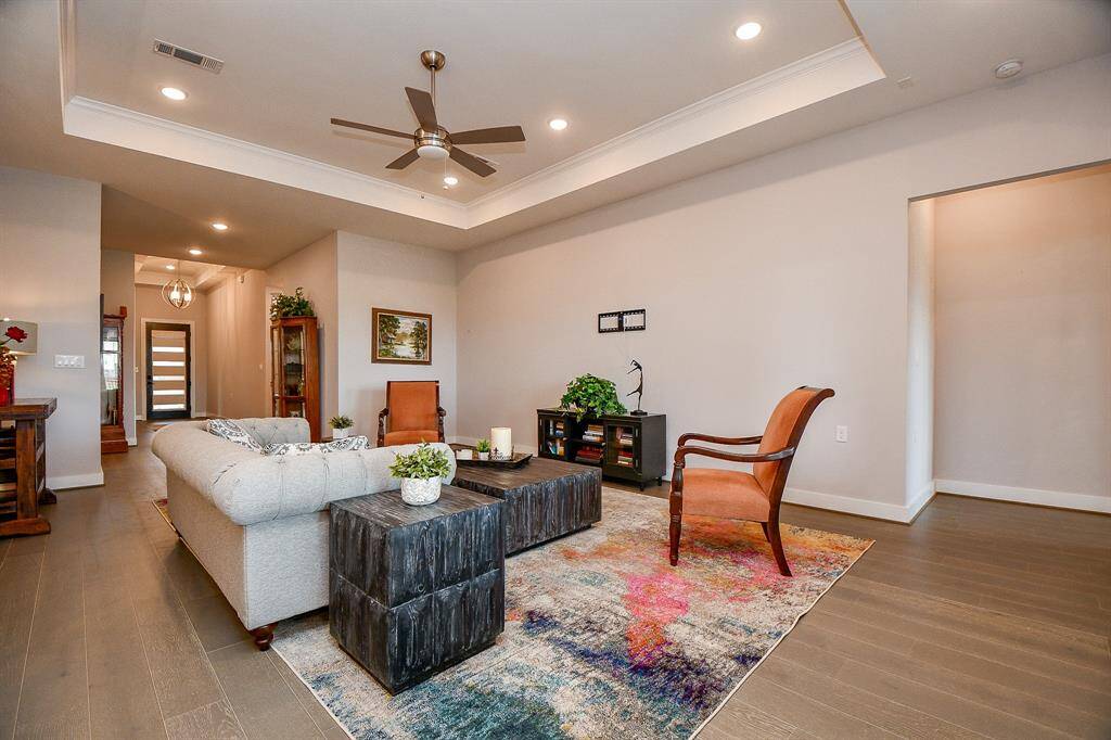 This photo showcases a bright, modern entryway with wood flooring and a stylish light fixture. It features a front door with vertical glass panels, an adjacent powder room, and a hallway leading further into the home.