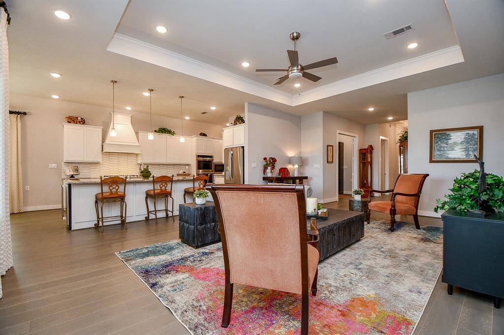 This inviting open-concept living space features elegant tray ceilings, warm wood flooring, and ample natural light. The area seamlessly connects to a modern kitchen with a central island, ideal for entertaining.