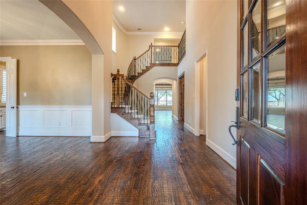 Step into the grand two-story entry, where a curved staircase with a wooden banister and intricate baluster design makes a striking first impression. A chandelier with frosted glass shades and swirl detailing casts a warm glow, while the wood tread and carpeted stairs add both elegance and comfort to this stunning foyer.