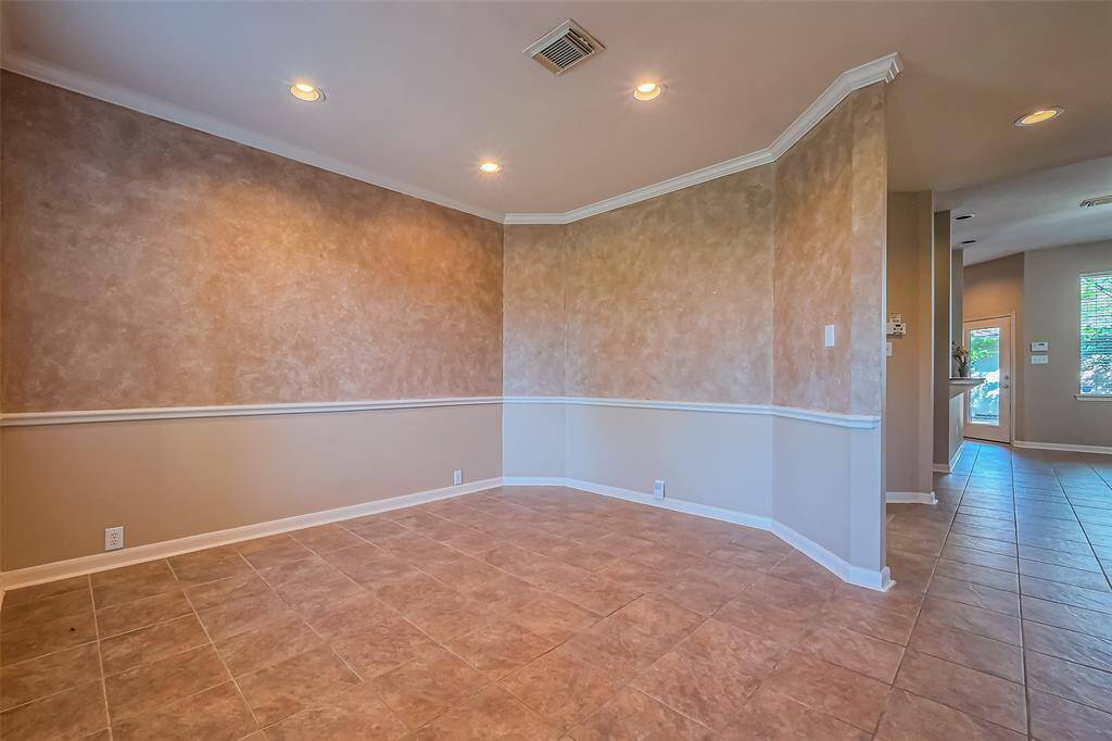 This photo showcases a sunlit dining room just off the entry, featuring warm-toned walls with elegant chair rail molding and classic tiled flooring. Recessed lighting adds a modern touch, while the open layout flows seamlessly into a connecting hallway, offering easy access to the rest of the home. A perfect blend of style and function, this space is ideal for both everyday dining and entertaining.