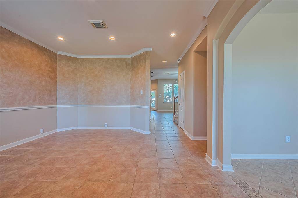 This photo highlights a beautifully spacious open-concept interior featuring timeless tiled floors, soft neutral walls, and recessed lighting for a clean, modern feel. The hallway draws you into a bright, airy room filled with natural light from large windows—creating a warm and welcoming atmosphere perfect for everyday living or entertaining.