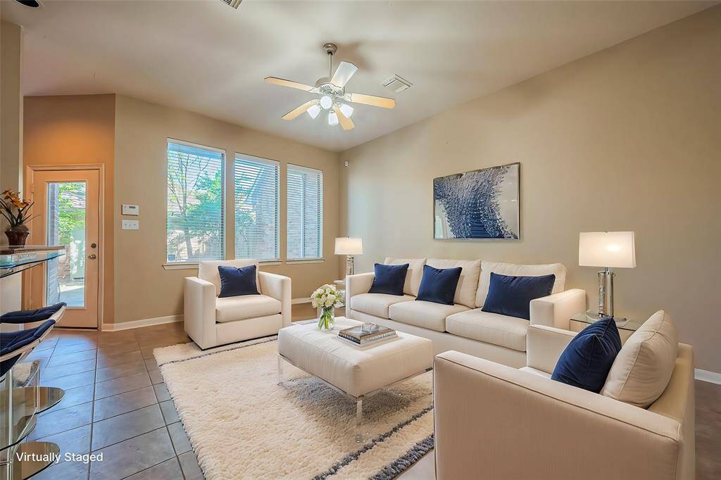 This photo shows a bright and inviting living room with high ceilings and large windows. A ceiling fan and contemporary virtually staged decor complete the space, offering unlimited possibilities for either a traditional, or a modern and cozy atmosphere.