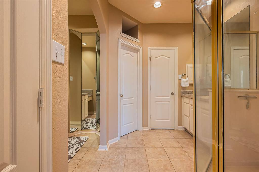 Step into this bright and inviting bathroom featuring soft beige walls, classic tiled flooring, and warm recessed lighting that creates a serene ambiance. The space includes a sleek glass walk-in shower and a stylish vanity area topped with a beautiful granite countertop. Thoughtfully designed for functionality and comfort, the primary suite also offers two spacious primary His and Hers closets—providing ample storage and organization.
