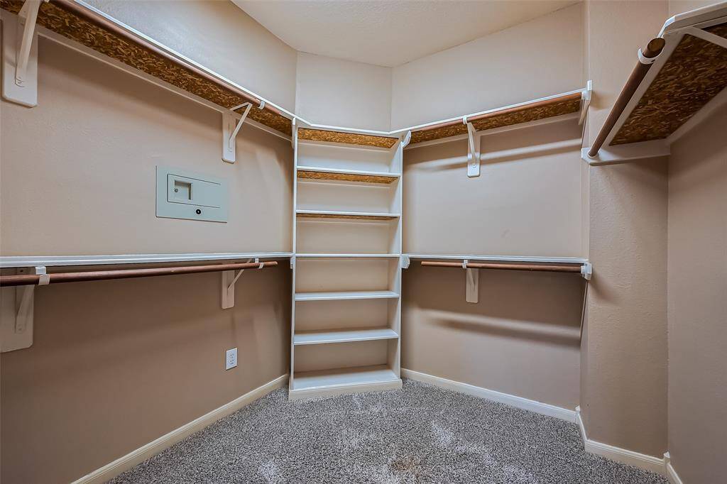 This is one of the two  spacious walk-in closets in the primary suite featuring multiple hanging rods and open shelving, with a neutral color palette and carpeted floor, perfect for ample storage and organization.