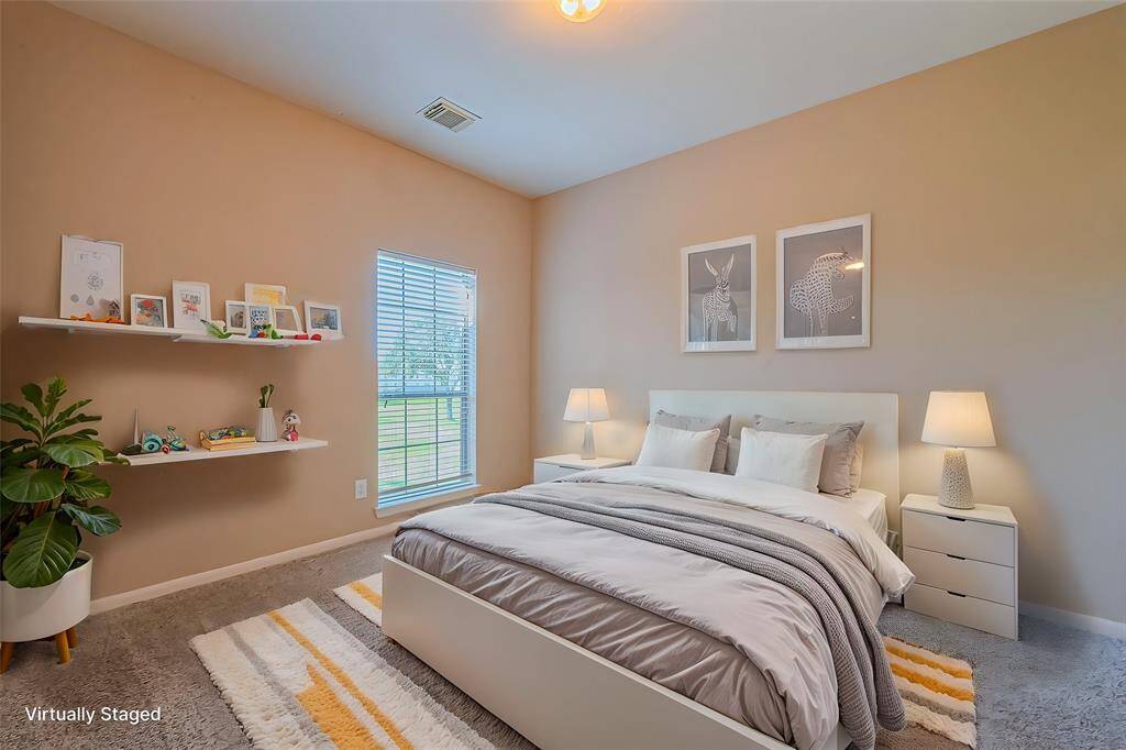 This spacious bedroom features neutral walls, a ceiling fan, and plush carpeting. It has ample natural light from two large windows and offers access to a bathroom through an open doorway.