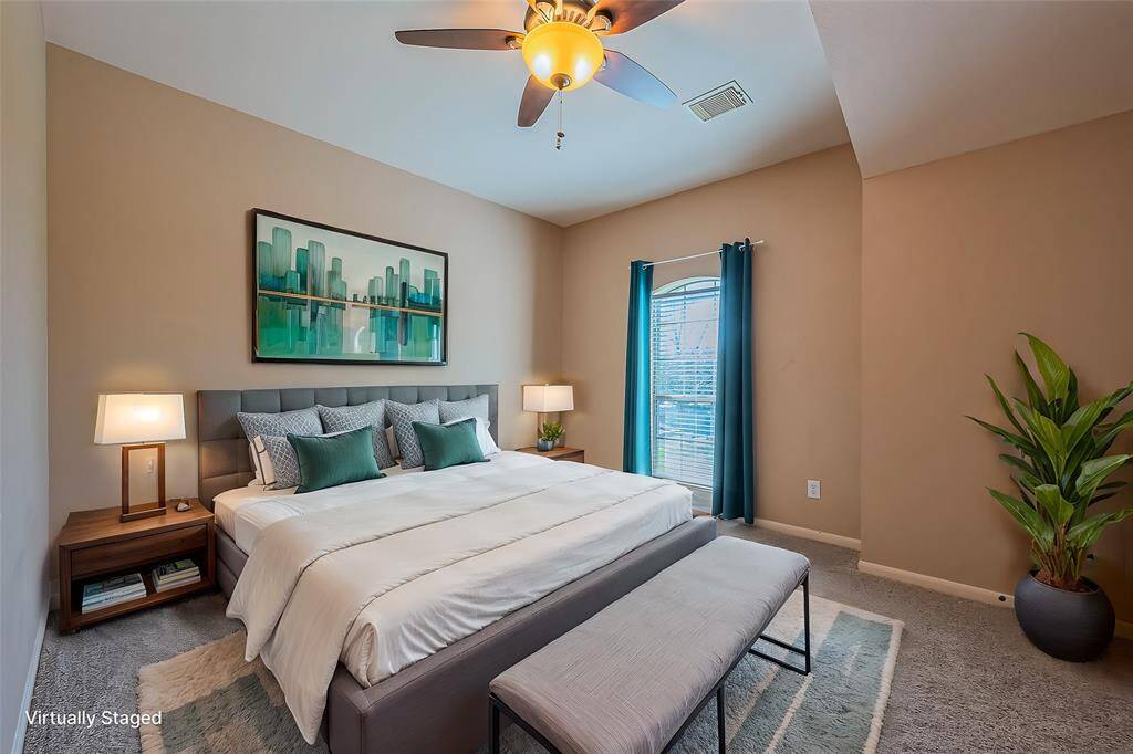Spacious bedroom featuring neutral-toned walls, large window with natural light, and a ceiling fan with light fixture. Plush carpet flooring and ample wall space provide flexibility for furniture layout.
