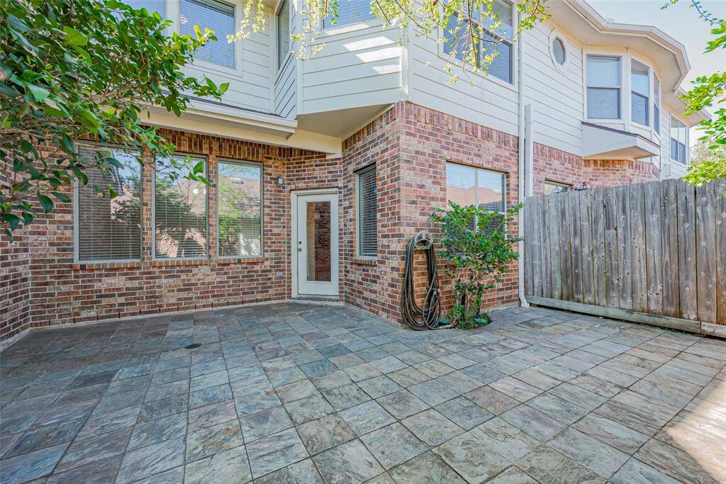 This photo showcases a quaint brick courtyard patio area with ample natural light, surrounded by a wooden fence for privacy. The space provides a seamless indoor-outdoor flow, ideal for relaxation or entertaining.