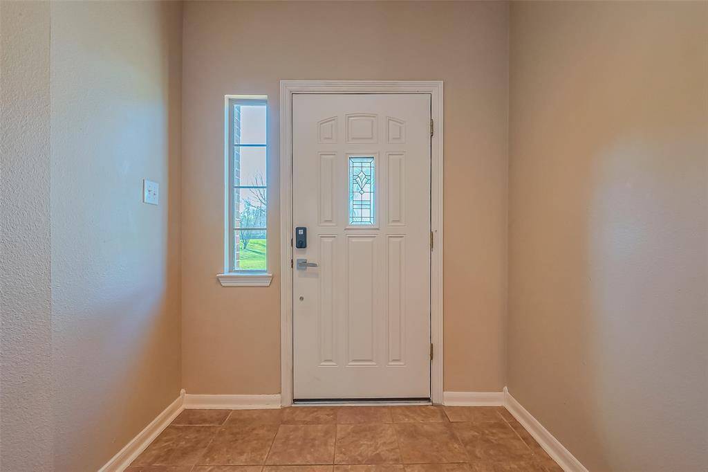 This photo showcases a welcoming entryway with a white front door featuring decorative glass. The space is accented by a narrow window, allowing natural light to brighten the neutral-toned walls and tiled floor.