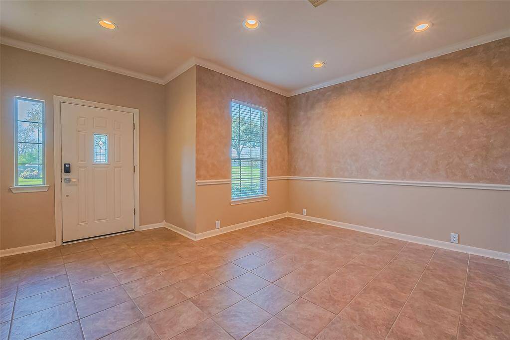 Bright and spacious room with tiled floors, neutral walls, and recessed lighting. A large window invites natural light, while the elegant front door with decorative glass panels creates a welcoming entryway.