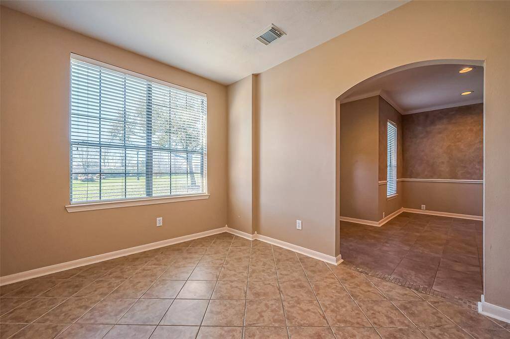 This photo showcases a bright, tiled room with neutral walls and a large window that fills the space with natural light. An elegant arched entryway leads to entry foyer area, enhancing the open and airy feel. Whether used as a second living area, home office, or creative space, this room offers endless possibilities to suit your lifestyle.