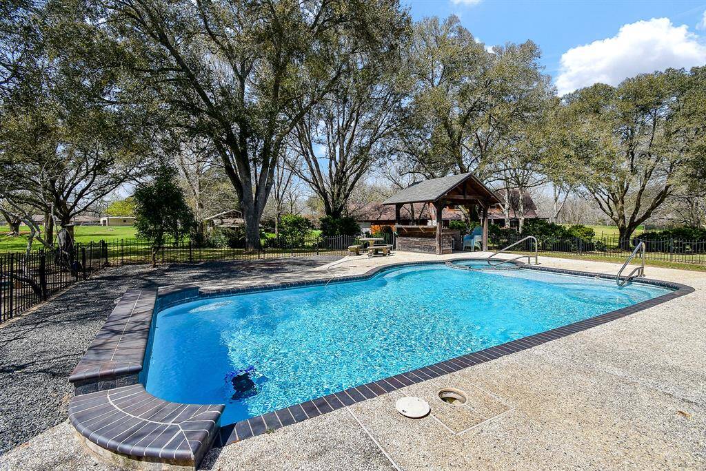 Here’s another view of this sparkling pool and spa. You can see the charming patio table and benches, as well as the outdoor kitchen. The pool is fully fenced, providing added safety for the area.