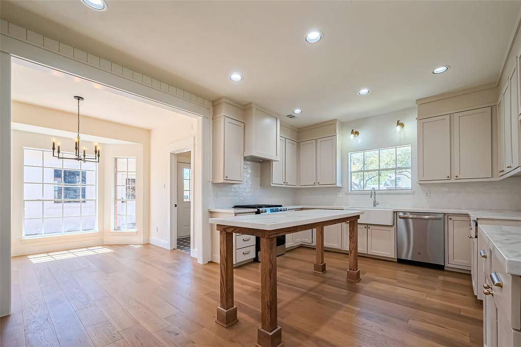 This modern kitchen, boasts sleek painted cabinetry, a custom island, quartz counters, and a farmhouse sink with floating shelves and a built in pantry.
