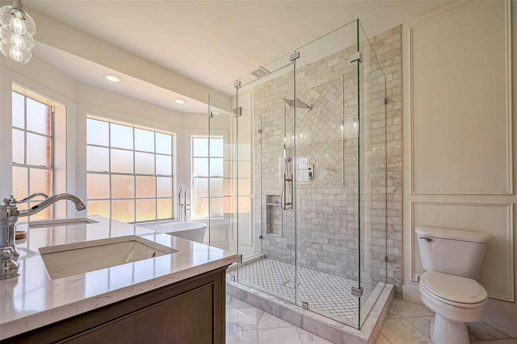 Elegant primary bathroom featuring a new vanity, stand-alone tub, marble floors, and shower with a frameless shower glass door and a shiplab wall.