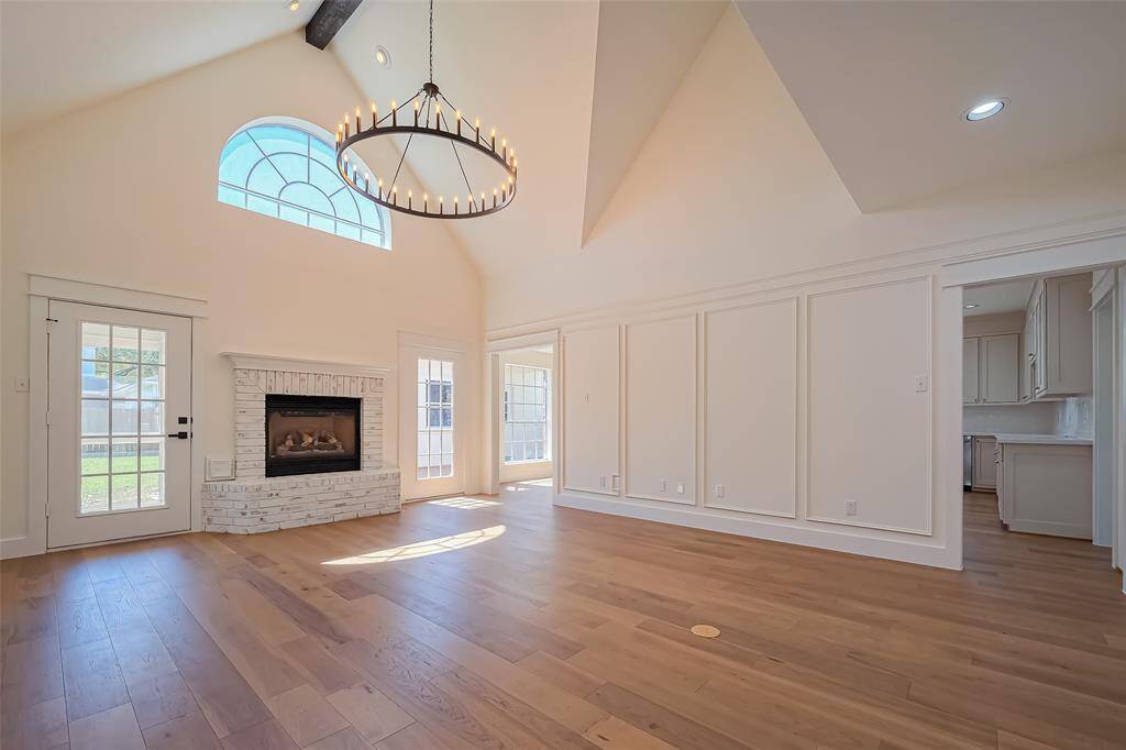 Discover the perfect blend of elegance and comfort in this airy family room, boasting high ceilings, a sleek modern chandelier, and engineered wood floors.