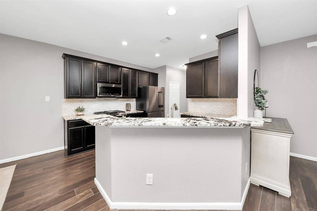 Culinary haven, featuring granite countertops, a tile backsplash, stainless steel appliances, and 42” upper cabinets.
