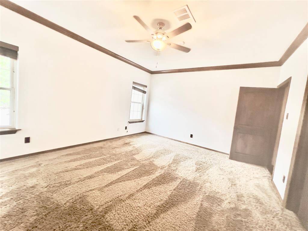 This is a spacious, brightly-lit room with textured carpeting, a slanted ceiling with a ceiling fan, and two windows providing natural light. It features a neutral color palette, ready for personalization.