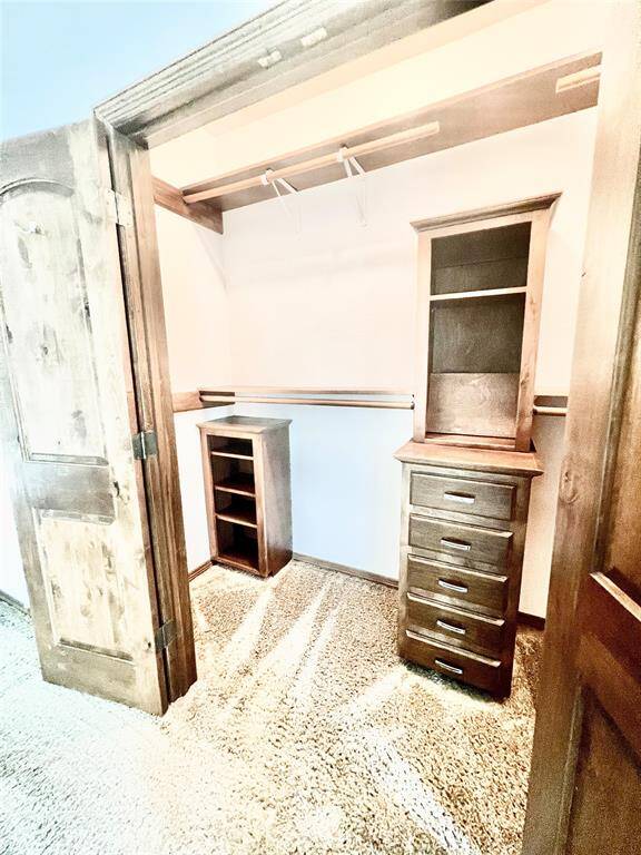 This is a cozy, carpeted walk-in closet featuring built-in wooden shelving and drawers, providing ample storage space. The rustic-style sliding door adds a charming touch to the room.