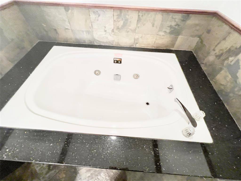 The photo shows a modern corner jacuzzi bathtub with multiple jets and sleek fixtures, set against a marbled wall and on a speckled dark countertop. Perfect for a relaxing soak in a contemporary bathroom setting.